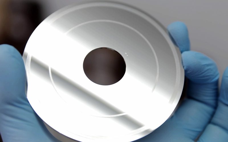 Eldivenli elde tutulan, yüzeyinde dairesel izler bulunan hard disk plakası