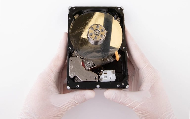 Eldivenli ellerde kapağı açılmış, plakasında sıvı lekeleri görünen su hasarlı 3.5 inç hard disk